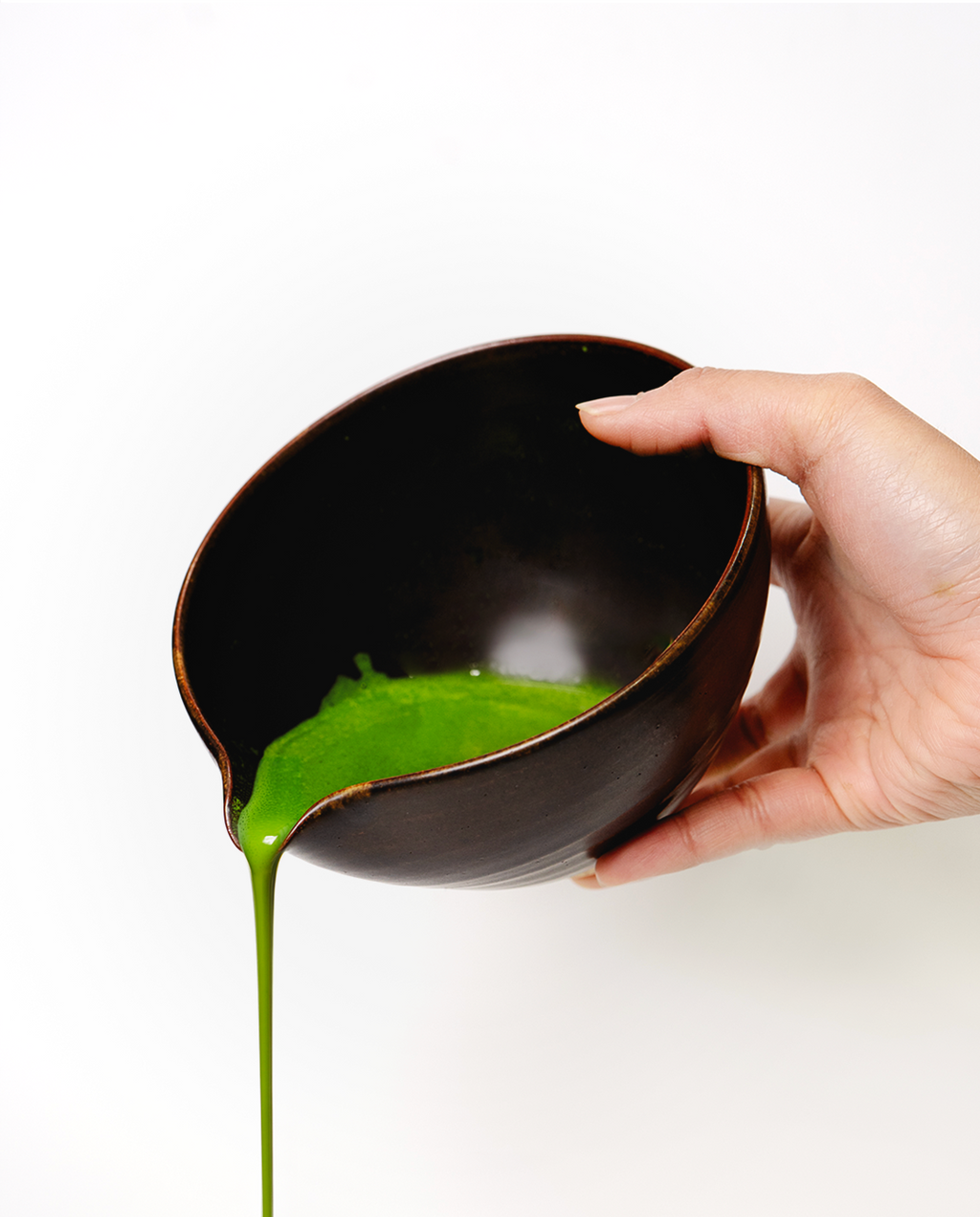Hand holding a black bowl with Matcha pouring out on a white background