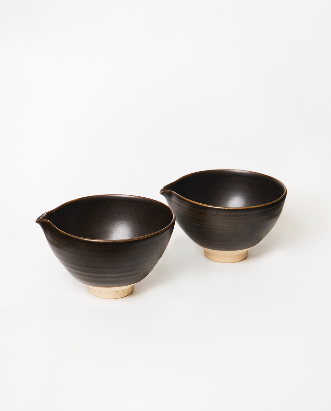 Two black ceramic bowls with beige bases on a white background
